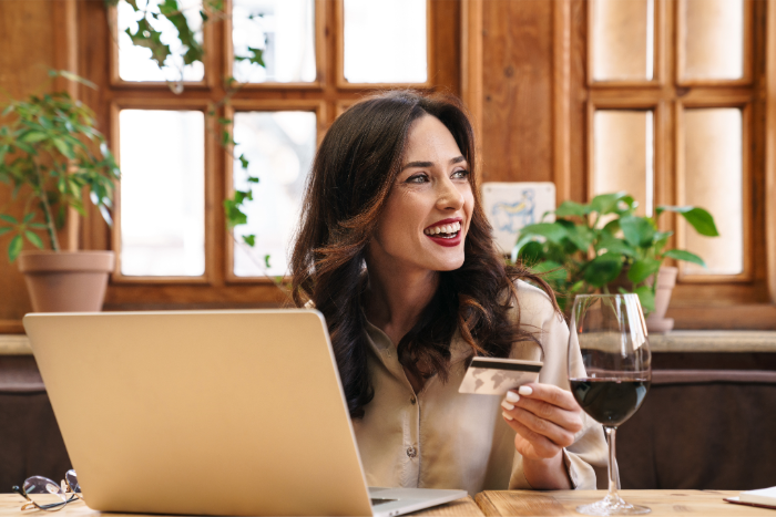 A woman paying for wine with a credit card on her laptop with a glass of wine 