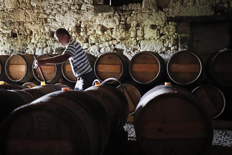 Château Le Puy barrels in the cellar with a worker testing the wine