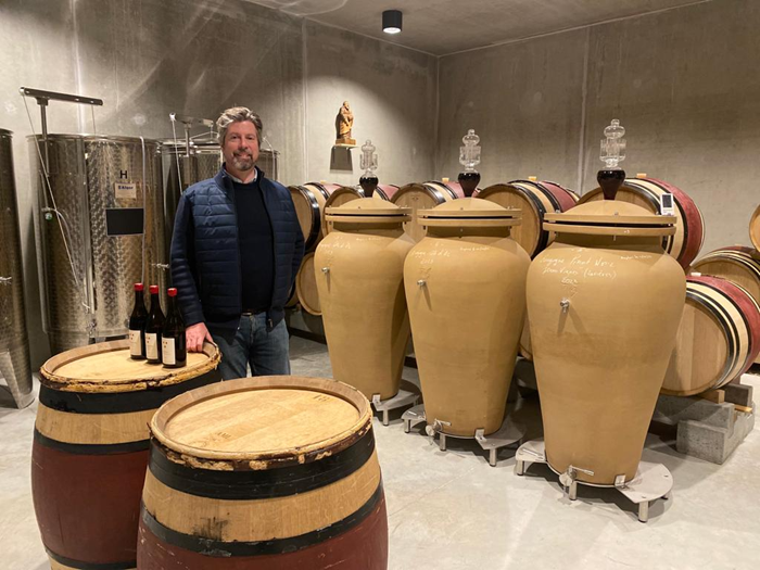 Antoine Lepetit de la Bigne in his cellar surrounded by amphora and wooden barrels with three bottles of his wine