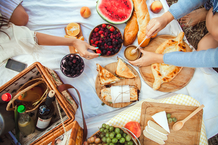people around a picnic mat with an array of food and wine